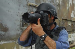 A press photojournalist is holding a camera with a zoom lens and is photographing war and conflict.